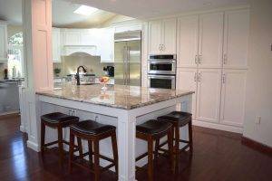 tall white themed kitchen with long white cabinets and a marble island with stools built and installed by Creation Cabinetry in Hamburg PA