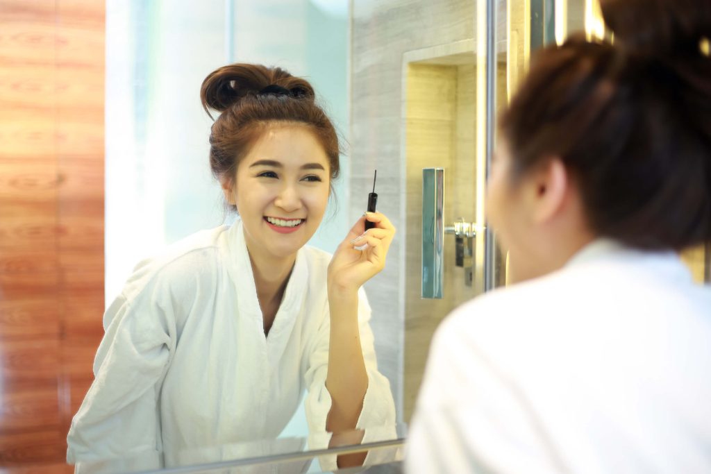 woman smiling in mirror and applying makeup, bathroom storage for makeup